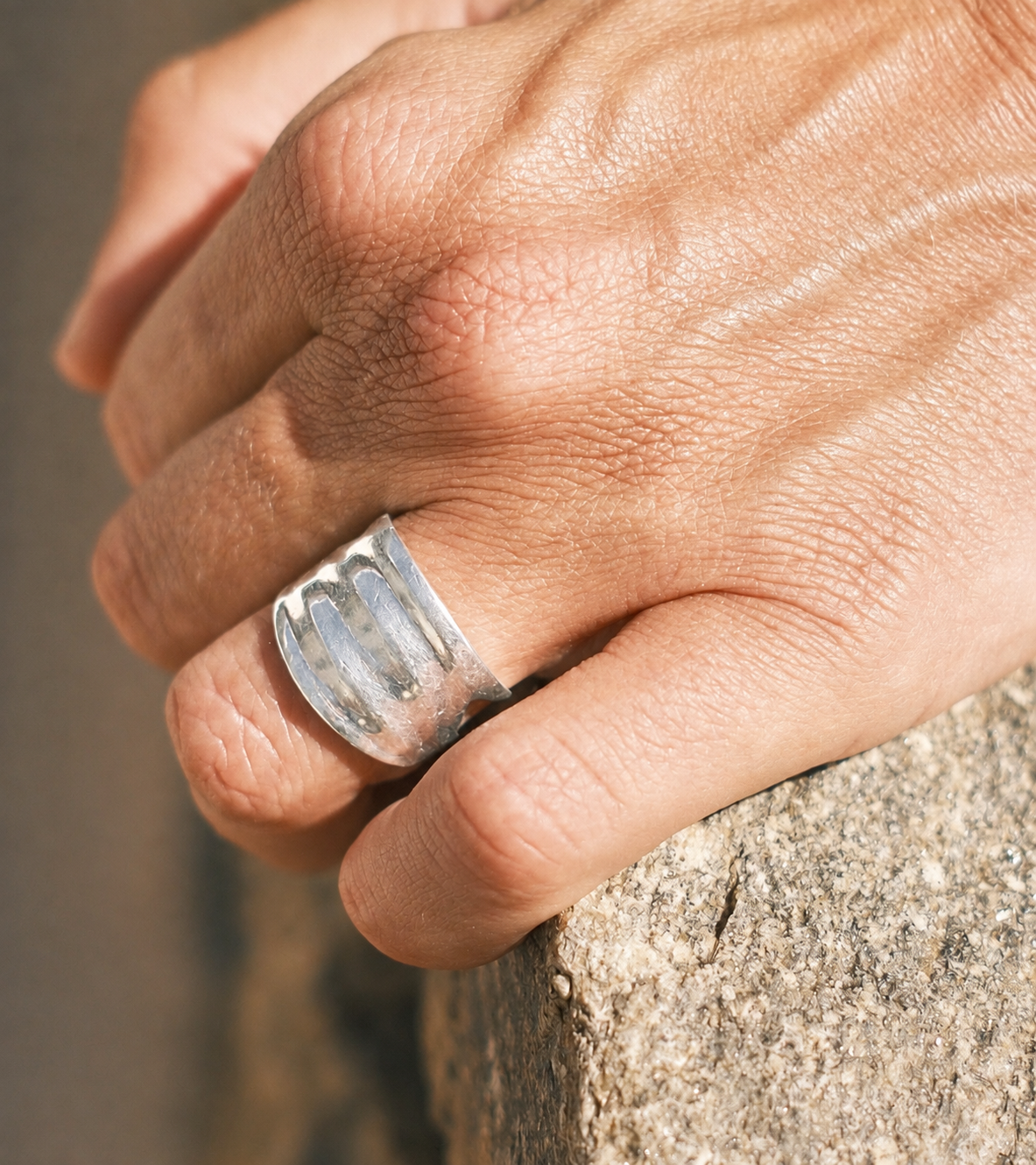 Close-up of a sculptural silver ring worn against a stone surface